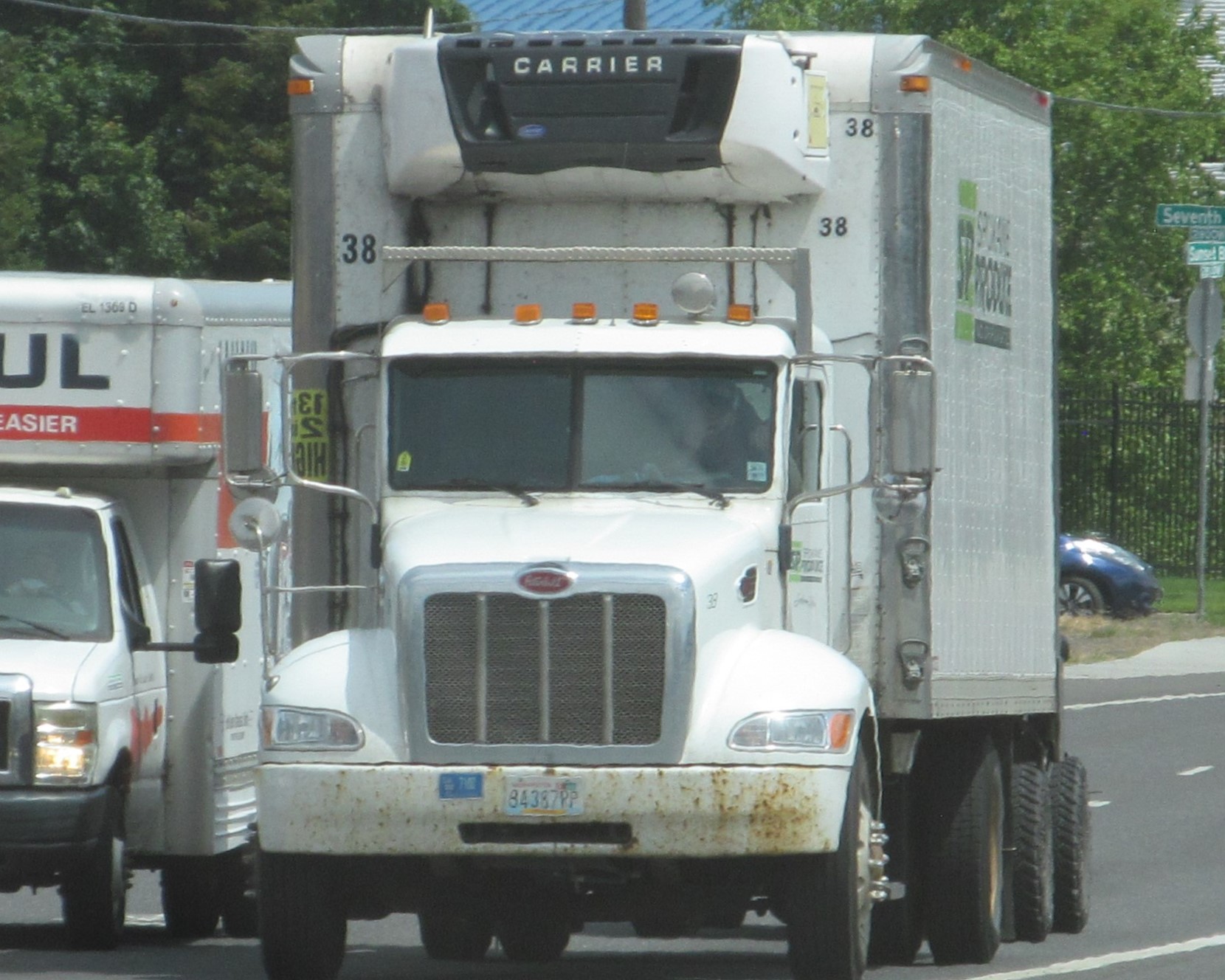 A white Peterbilt tractor pulling a refrigerated produce trailer, seen from the front at a stoplight