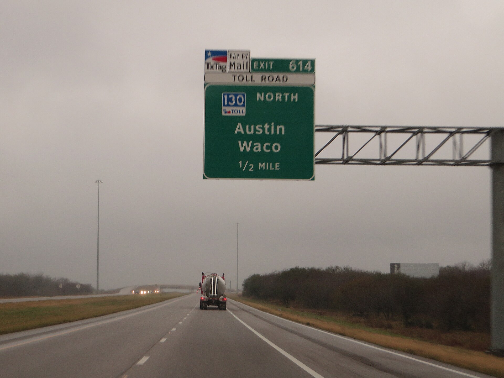 A tanker truck driving on Interstate 10 in Texas beneath an overhead sign for the SH 130 toll road exit toward Austin and Waco