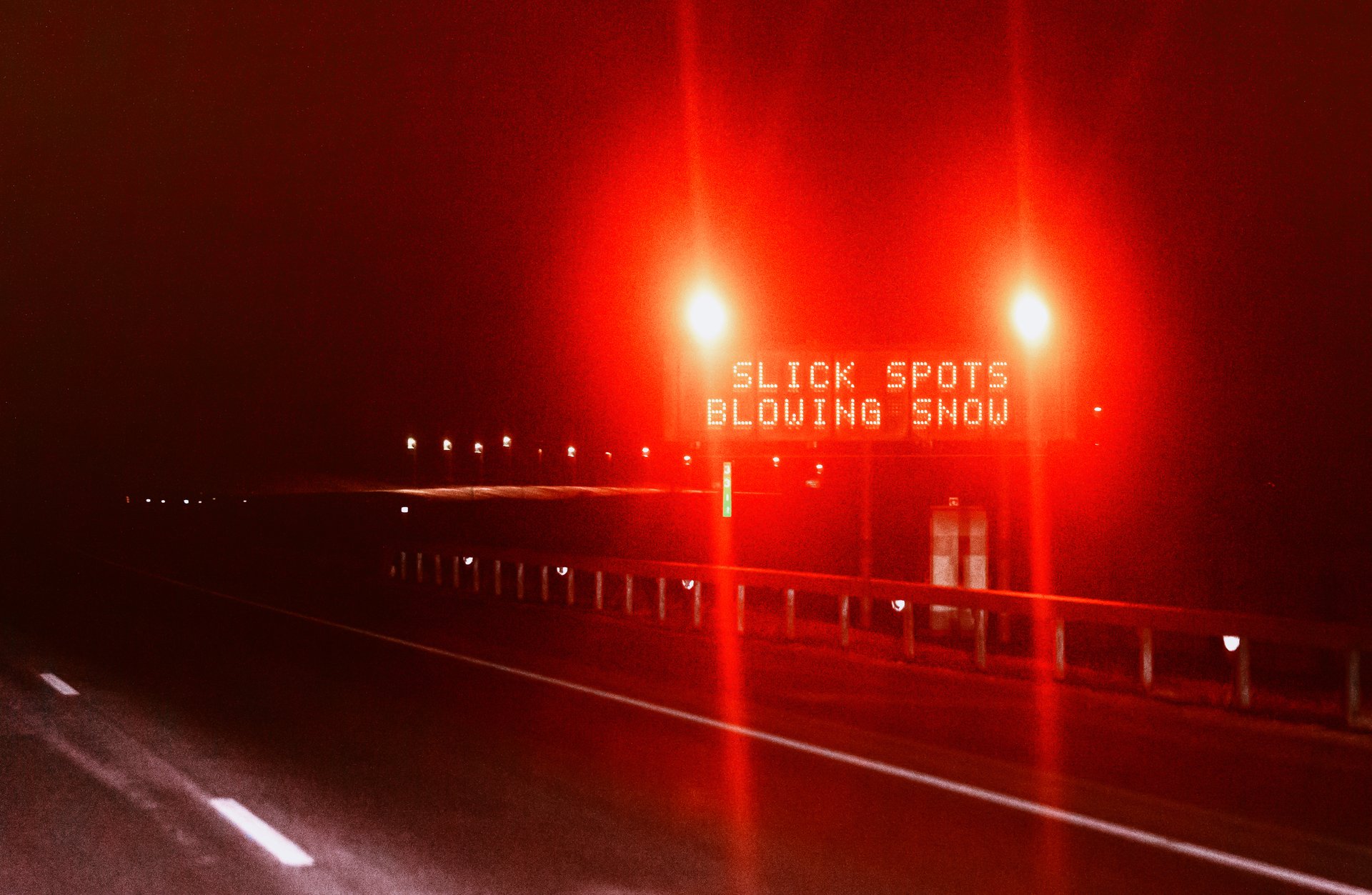 An electronic highway sign lit red at night reading 'Slick Spots Blowing Snow' over a dark, empty stretch of Interstate 80 near Buford, Wyoming