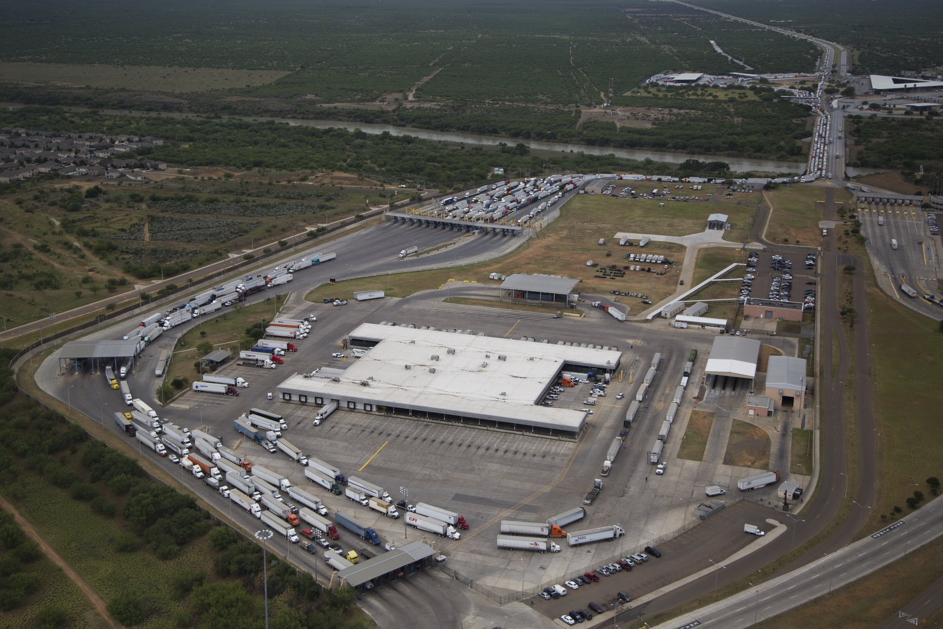 Aerial view of the World Trade Bridge truck inspection facility in Laredo, Texas, with long lines of semi trucks queuing for inspection and the Rio Grande in the background