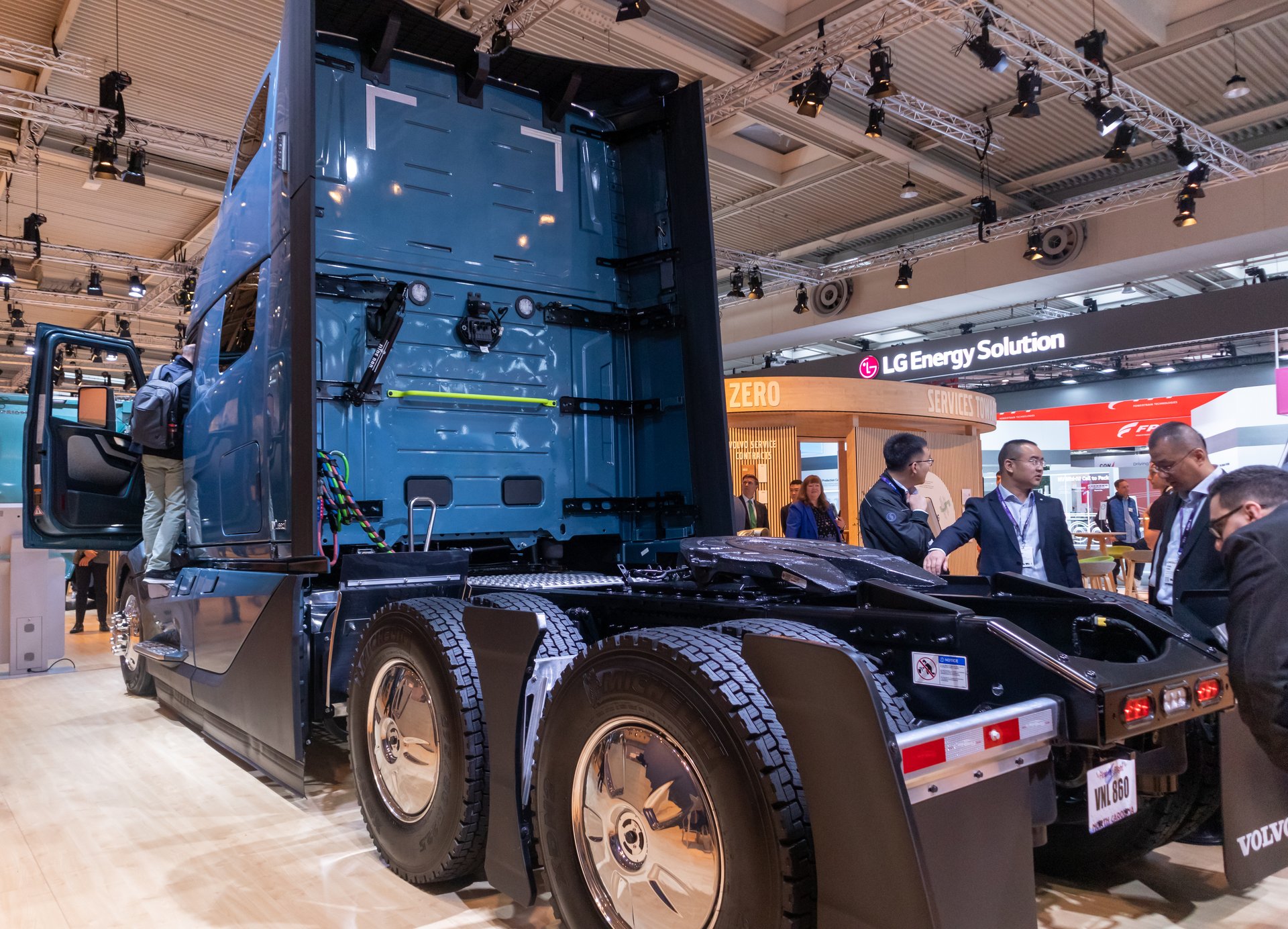 The back of a blue Volvo VNL 860 sleeper cab on display at a trade show, showing the cab rear, chassis and fifth wheel
